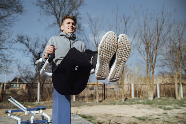 Young man doing sit-ups on bars outdoors.Fitness man doing exercise on bars outdoor. - Foto, afbeelding