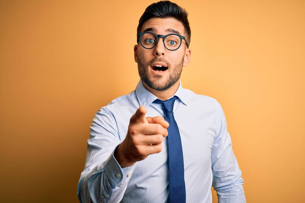 Young handsome businessman wearing tie and glasses standing over yellow background pointing displeased and frustrated to the camera, angry and furious with you - Photo, Image