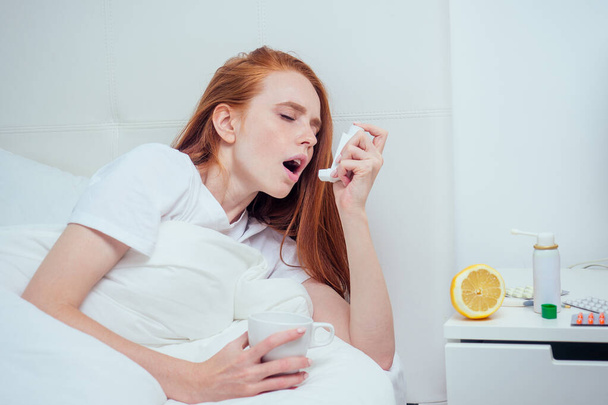 Рыжая рыжая женщина, завернутая в одеяло и чувствующая себя плохо настроение, потому что она грипп инфекции с помощью ингалятора астмы
 - Фото, изображение