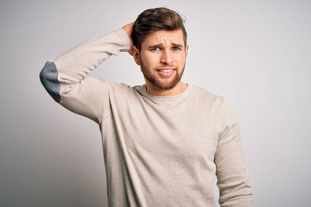 Young handsome blond man with beard and blue eyes wearing casual sweater confuse and wonder about question. Uncertain with doubt, thinking with hand on head. Pensive concept. - Photo, Image