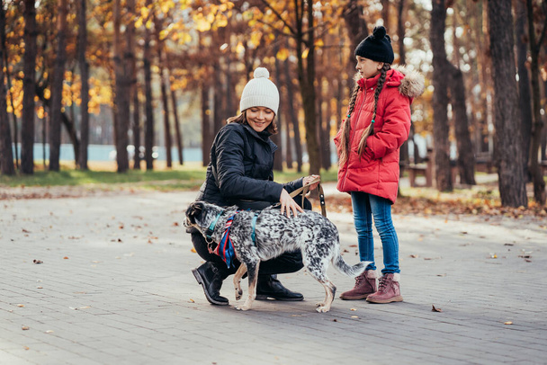 Feliz madre y su hija jugando con el perro en el parque de otoño
 - Foto, Imagen