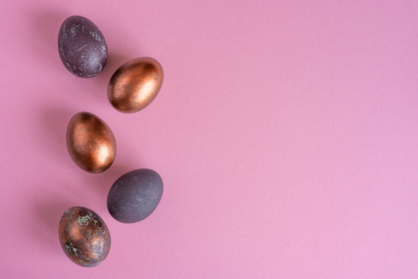 Colored painted pearl chicken eggs of violet, golden color on pink background. Minimalistic creative idea - Zdjęcie, obraz