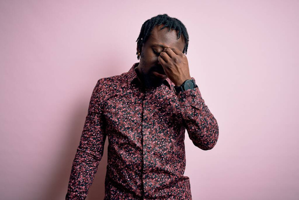 Mladý pohledný africký Američan v neformální košili stojící nad růžovým pozadím unavený mnul nos a oči pocit únavy a bolesti hlavy. Koncept stresu a frustrace. - Fotografie, Obrázek