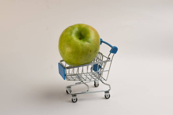 Green apple in a supermarket trolley on a white background - Foto, afbeelding