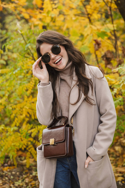 Beautiful young cheerful woman wearing coat walking in the autumn park - Fotografie, Obrázek