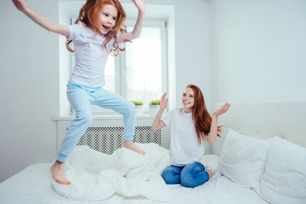 mom and girl are jumping on the bed at home. success concept - Foto, Bild