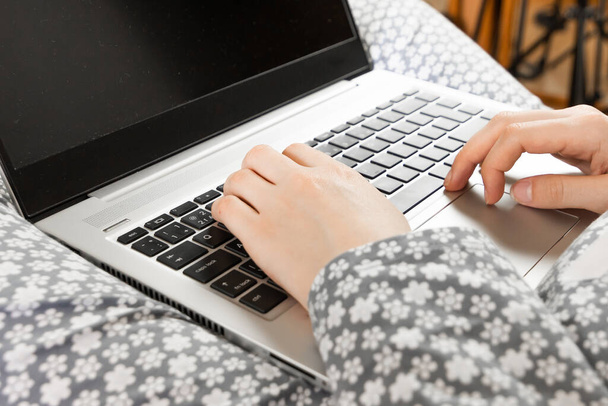 Frontansicht auf dem Bildschirm eines Laptops auf den Knien einer Frau in grau geblümter Nachtwäsche. Home Office Konzept. Freiberuflerin arbeitet bei Ausbruch des Coronavirus im Bett. - Foto, Bild