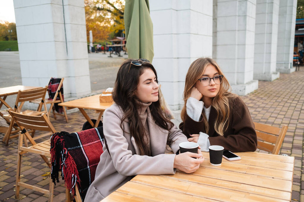 Two attractive women friends sitting at the cafe outdoors, drinking coffee - Photo, Image