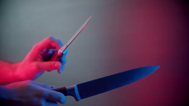 Πρόσωπο που κρατά και ακονίζει μαχαίρια μεταξύ τους σε φωτισμό νέον - Πλάνα, βίντεο
