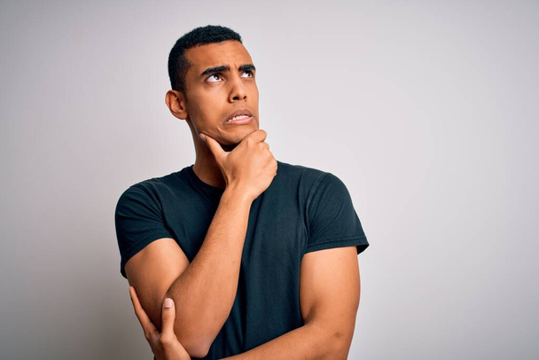 Young handsome african american man wearing casual t-shirt standing over white background Thinking worried about a question, concerned and nervous with hand on chin - Fotó, kép