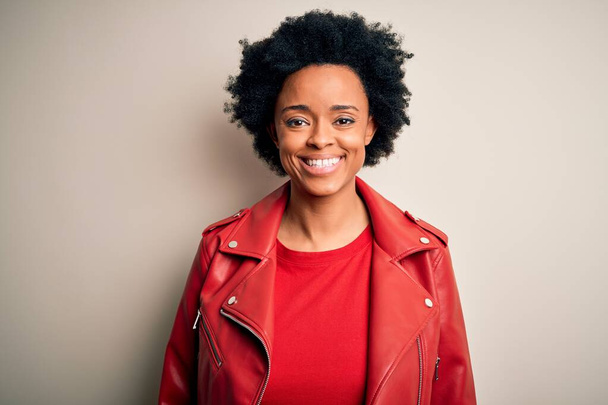 Junge schöne afroamerikanische Afro-Frau mit lockigem Haar trägt lässig rote Jacke mit einem fröhlichen und kühlen Lächeln im Gesicht. Glücklicher Mensch. - Foto, Bild
