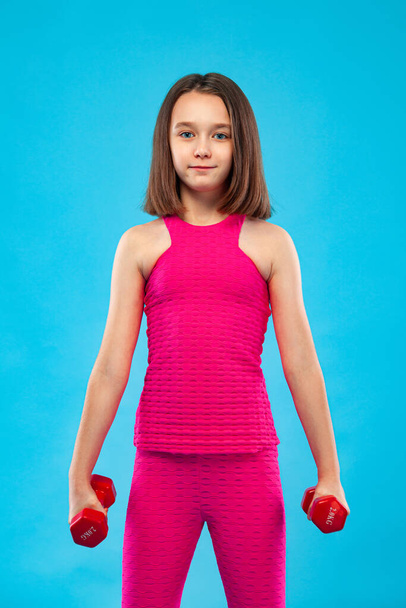 Kid girl doing fitness exercises with dumbbells on blue background - Φωτογραφία, εικόνα