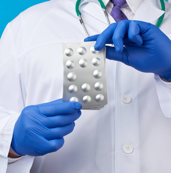 mano masculina con guantes estériles azules sostiene una pila de píldoras en una ampolla, concepto para el tratamiento farmacológico de enfermedades, fondo azul
 - Foto, imagen