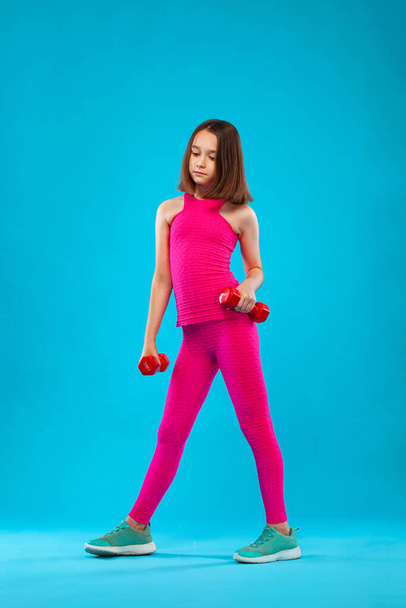 Kid girl doing fitness exercises with dumbbells on blue background - 写真・画像