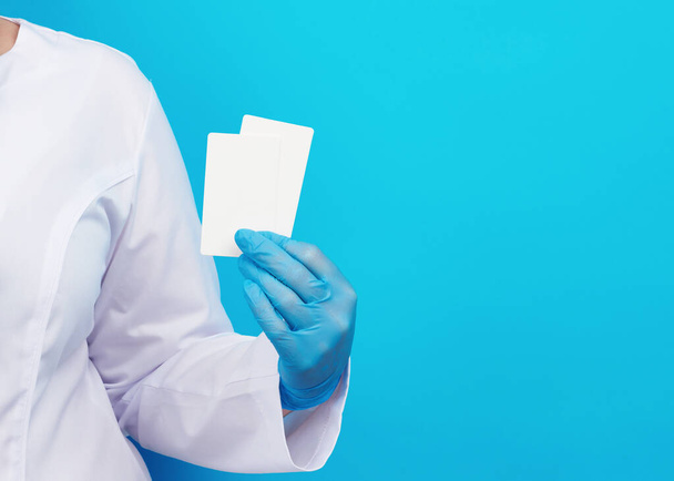 doctor hand in blue medical latex gloves holds an empty paper business card on a blue background, place for an inscription - Фото, зображення