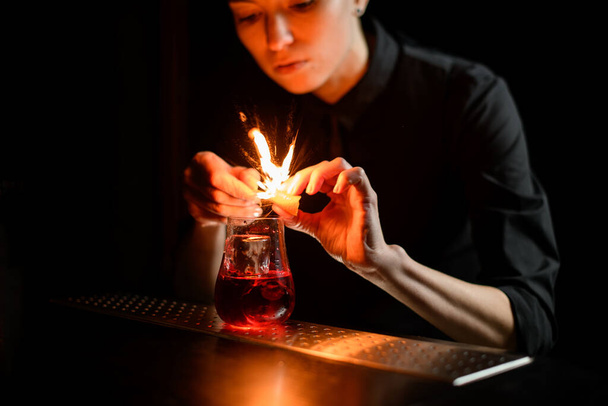 close-up barman gently sprinkles on glass with red cocktail and ice and make fire. - Foto, Bild