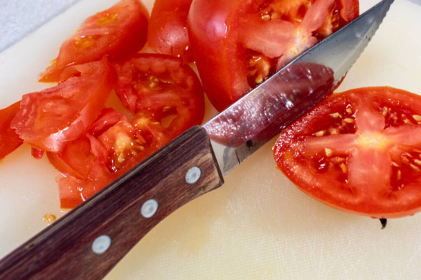 Een steakmes met een houten handvat snijdt door een rode biefstuk tomaat op een snijplank. - Foto, afbeelding