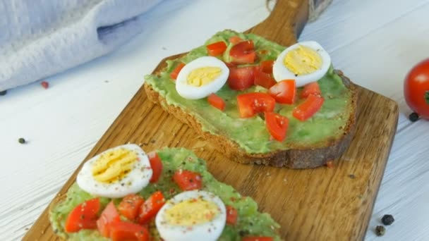 Healthy Vegan food. Spread mashed avocado on toasted brown bread sprinkled with black and red pepper. Making tasty avocado toast for breakfast. Cooking bruschetta with cherry tomatoes and quail eggs. - Footage, Video