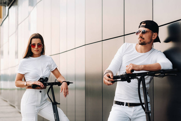 Ein Mädchen und ein Mann laufen auf Elektrorollern durch die Stadt, ein verliebtes Paar auf Motorrollern. - Foto, Bild