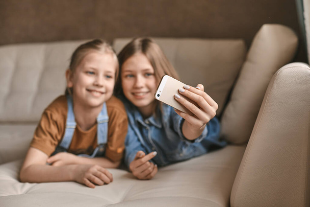 Meninas bonitas tirar selfies em seu telefone enquanto deitado no sofá. Irmãs fazem uma pausa dos trabalhos de casa e tiram fotos durante a quarentena
 - Foto, Imagem