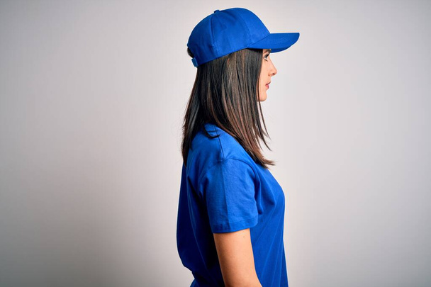 Fiatal futár nő kék szemű visel sapka felett kék háttér keres oldalra, pihenjen profil pózol természetes arc magabiztos mosollyal. - Fotó, kép