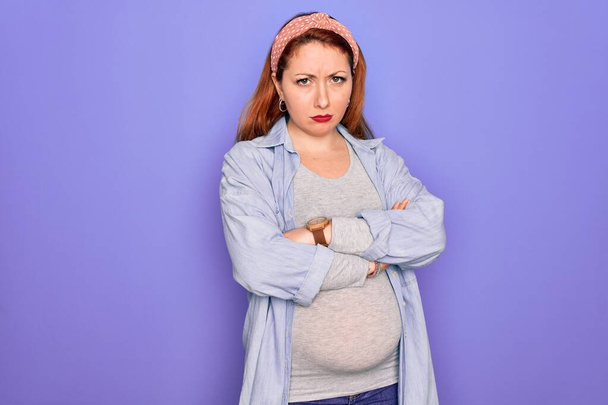 孤立した紫色の背景に赤ちゃんを期待している若い美しい赤毛の妊婦懐疑的で緊張し、両腕を組んで顔に不承認の表現。負の人. - 写真・画像
