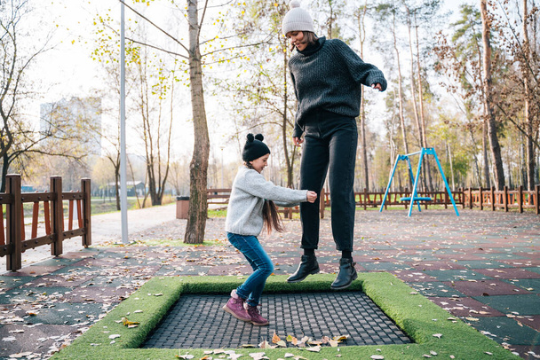 Mom and her daughter jumping together on trampoline in autumn park - Foto, Imagen