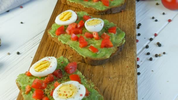 Healthy Vegan food. Spread mashed avocado on toasted brown bread with black and red pepper. Making tasty avocado toast for breakfast. Cooking bruschetta with cherry tomatoes and quail eggs. - Footage, Video