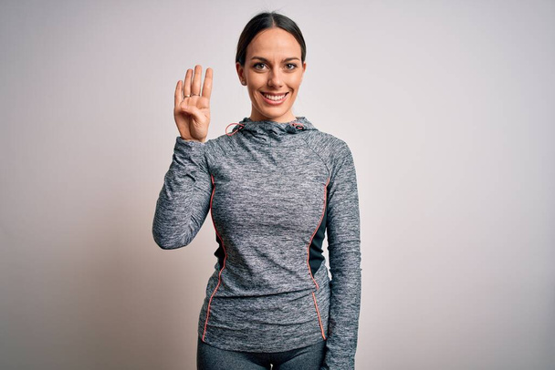 Giovane donna bionda fitness che indossa abiti sportivi su sfondo isolato mostrando e indicando con le dita il numero quattro sorridendo fiducioso e felice
. - Foto, immagini