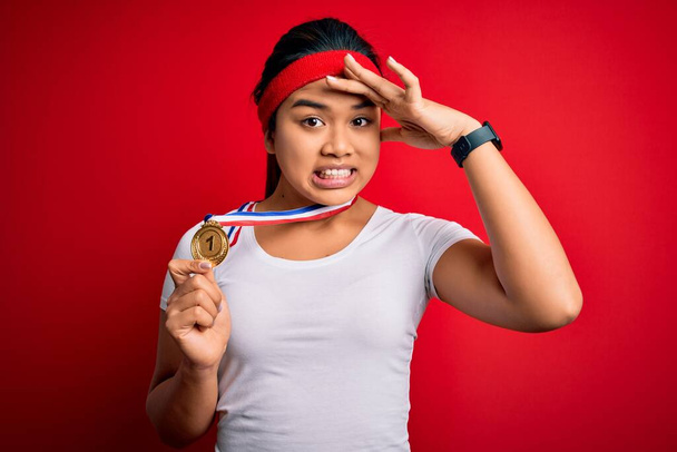 Genç Asyalı şampiyon kız, kırmızı arka planda madalyayı kazandı. Kafa kafaya vurularak, utanç ve şaşkınlık dolu, sinirli ve hayal kırıklığına uğramış bir şekilde. Hata için korku ve üzüntü. - Fotoğraf, Görsel