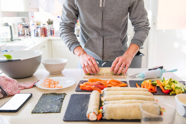 Cropped young caucasian man making sushi at home following cooking online video classes on website via smartphone. Internet technology for modern lifestyle concept. Soft selectove focus. Copy space - Foto, afbeelding