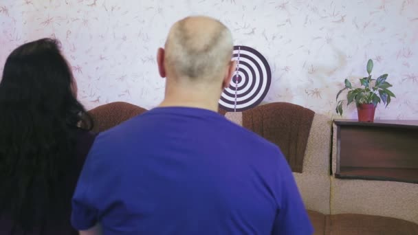 A woman and a man play darts at home in quarantine for the prevention of coranavirus - Materiał filmowy, wideo