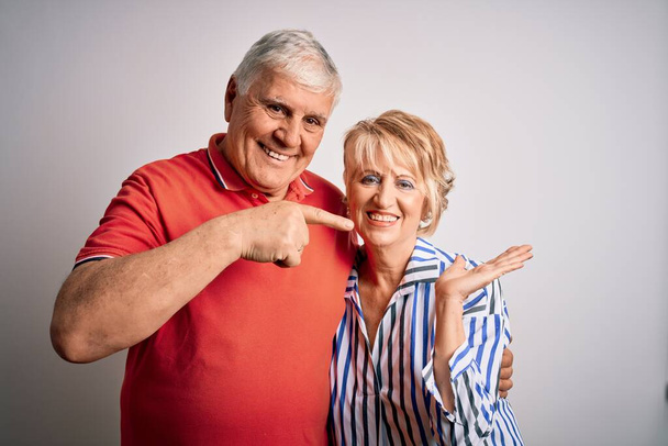 Senior beau couple debout ensemble sur fond blanc isolé étonné et souriant à la caméra tout en présentant avec la main et pointant du doigt
. - Photo, image