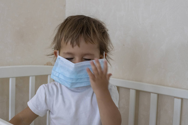 perheen turvallisuuskonsepti sepelvaltimoviruksen pandemiassa covid-19 pieni söpö lapsi laittaa lääketieteellisen naamion kasvoilleen seisten kotona vauvansängyssä.
. - Valokuva, kuva
