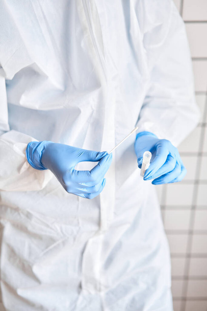2019-nCoV分析用の医師保持スワブ試験管。コロナウイルス検査。青い医療用手袋と保護面マスクは、 covid-19ウイルスから保護します。コロナウイルスとパンデミック. - 写真・画像
