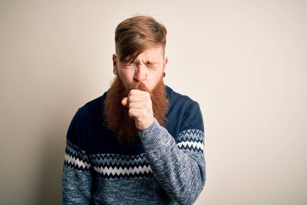孤立した背景感の上に冬のセーターを着て髭を生やしたハンサムなアイルランドの赤毛の男は具合が悪く、風邪や気管支炎の症状として咳をした。ヘルスケアの概念. - 写真・画像