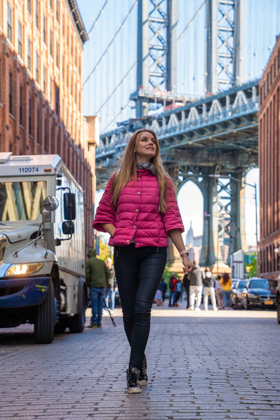 Fiatal gyönyörű hölgy sétál a Washington utcában, Brooklynban egy manhattani híddal a háttérben. - Fotó, kép