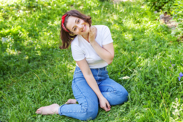Onnellinen tyttö hymyilee ulkona. Kaunis nuori brunete nainen ruskeat hiukset lepää puistossa tai puutarhassa vihreä ruoho tausta. Eurooppalainen nainen. Positiivinen ihmisen tunne kasvojen ilme kehon kieli - Valokuva, kuva