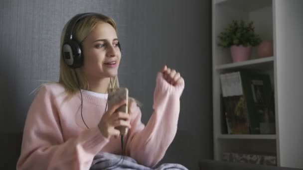 Close up of woman wearing headphones listening happy music and dancing on couch - Filmati, video