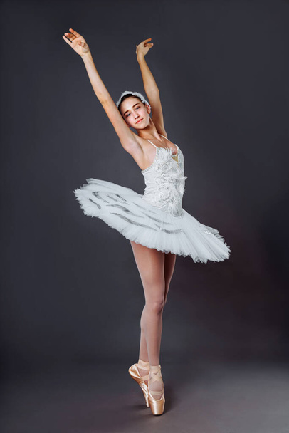 バレリーナは白いドレスで踊る。カラー写真。優雅なバレエダンサーまたは古典的なバレリーナダンスは、灰色のスタジオの背景に隔離されています。Ballerinaオンポイントシューズ足tutuからレイクスワン - 写真・画像