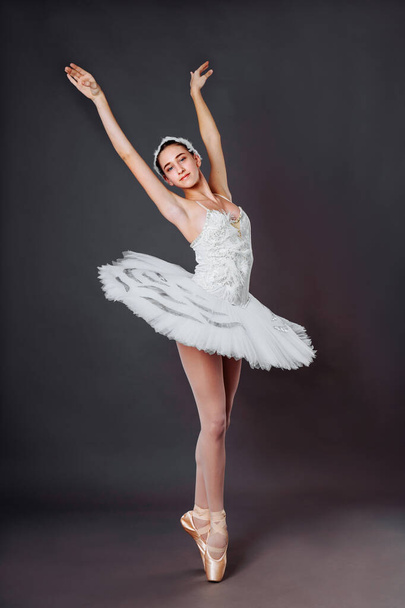 Portré fiatal gyönyörű kecses kaukázusi balerina gyakorolja balett pozíciók tütü szoknya fehér hattyú a hattyú-tó. Klasszikus balett táncos a stúdióban szürke háttér álló lábujjhegyen - Fotó, kép
