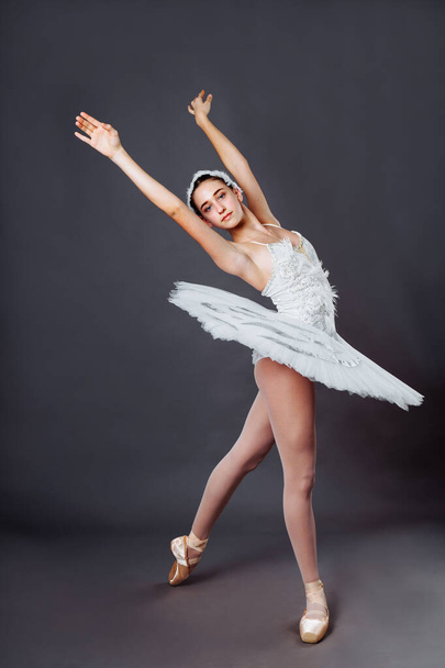 Porträt einer klassischen Balletttänzerin. Schöne anmutige Ballerina in weißem Tutu aus Schwanensee übt im Studio Ballett. Vertikales Bild eines hochbegabten jungen Teenagers in Spitze auf Hippies - Foto, Bild