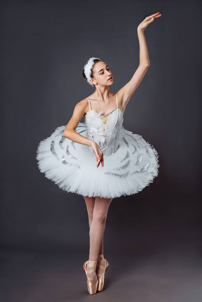 Ballerina dancing in white dress. Color photo. Graceful ballet dancer or classic ballerina dancing isolated on grey studio background. Ballerina on point shoes feet tutu from Lake Swan - Photo, Image