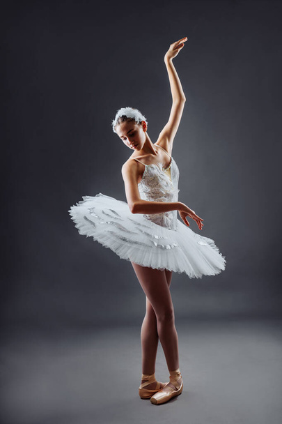 Балерина танцює в білій сукні. Color photo. Граціозний танцівник балету або класична балерина, що танцює ізольовано на сірому фоні студії. Балерина на точкових ногах туту з озера Лебедине - Фото, зображення