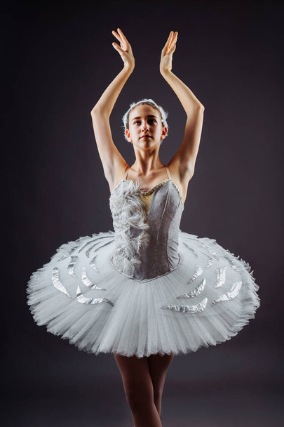 Eine junge grazile Ballerina in professioneller Kleidung, Spitzenschuhen und weißem Tutu demonstriert tänzerisches Können. Schöne klassische Balletttänzerin isoliert auf grauem Hintergrund im Fotostudio - Foto, Bild