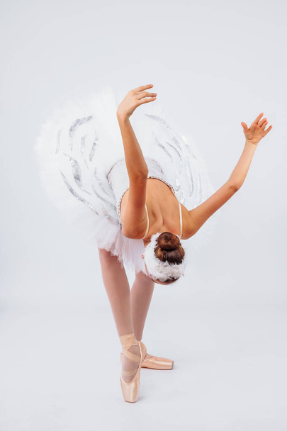 Привлекательная молодая балерина с красивым телом в трико танцует на цыпочках в фотостудии изолированы на белом фоне. Показывая красоту такого классического искусства, как балет
. - Фото, изображение