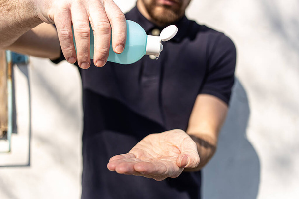 Hand sanitizer alcohol gel rub clean hands hygiene prevention of coronavirus virus outbreak. Man using bottle of antibacterial sanitiser soap. Outside on the street with sunshine and shadows. - Photo, Image