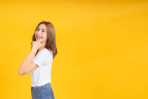 Portrait happy young asian woman looking camera finger pointing gesture presentation any product joyful funny positive emotion in white t-shirt, Yellow background isolated studio shot and copy space. - Photo, Image