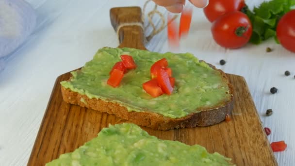Spread mashed avocado on a toasted brown bread. Making tasty avocado toast for breakfast. Cooking bruschetta with cherry tomatoes. Healthy Vegan food - Footage, Video