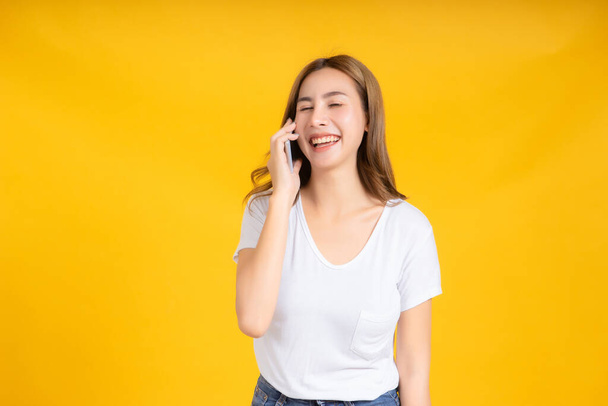 Portrait happy young asian woman talking conversation with smartphone, mobile phone positive emotion in white t-shirt, Yellow background isolated studio shot and copy space. - 写真・画像